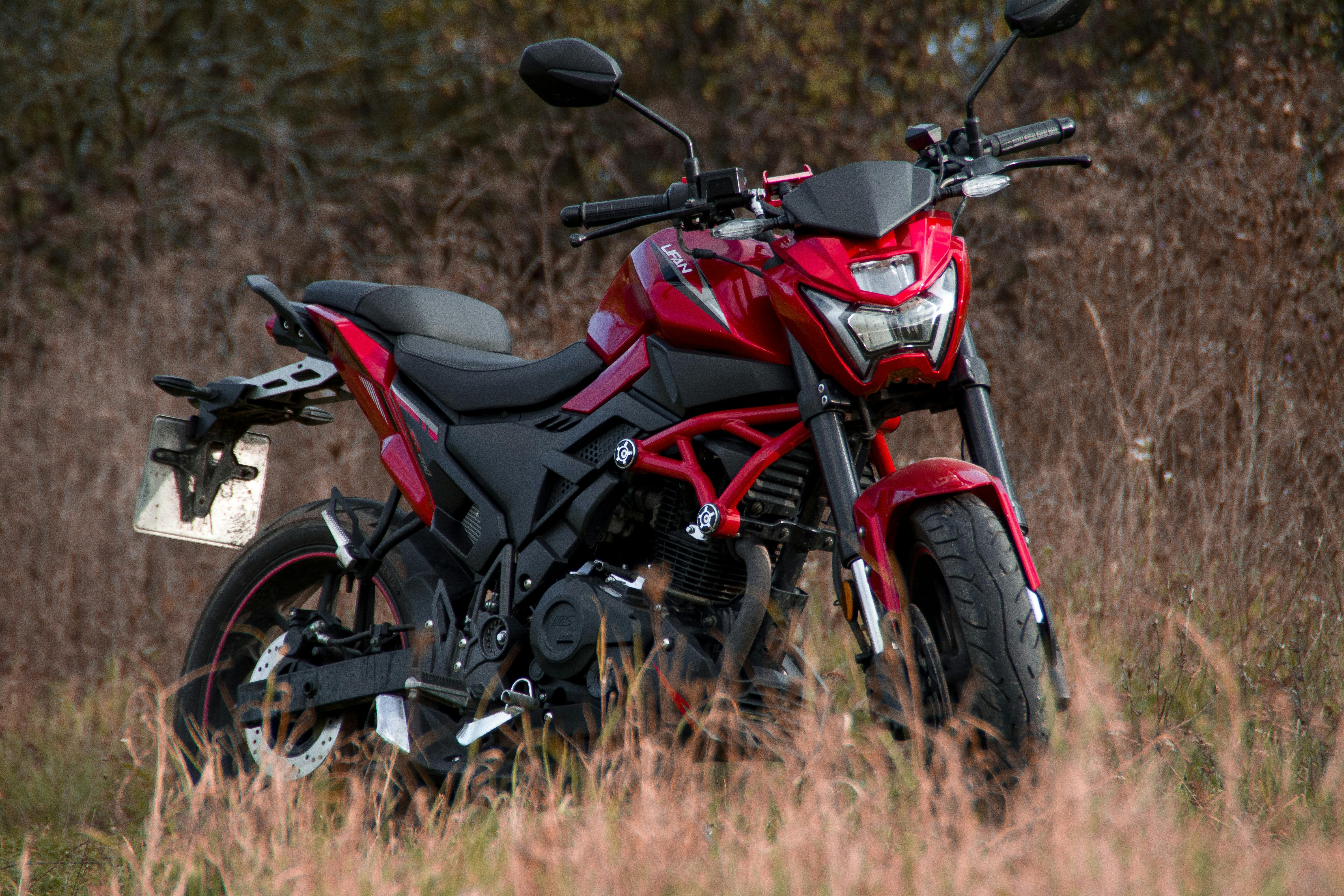 A red motorcycle parked in a dry grass field on a sunny day.