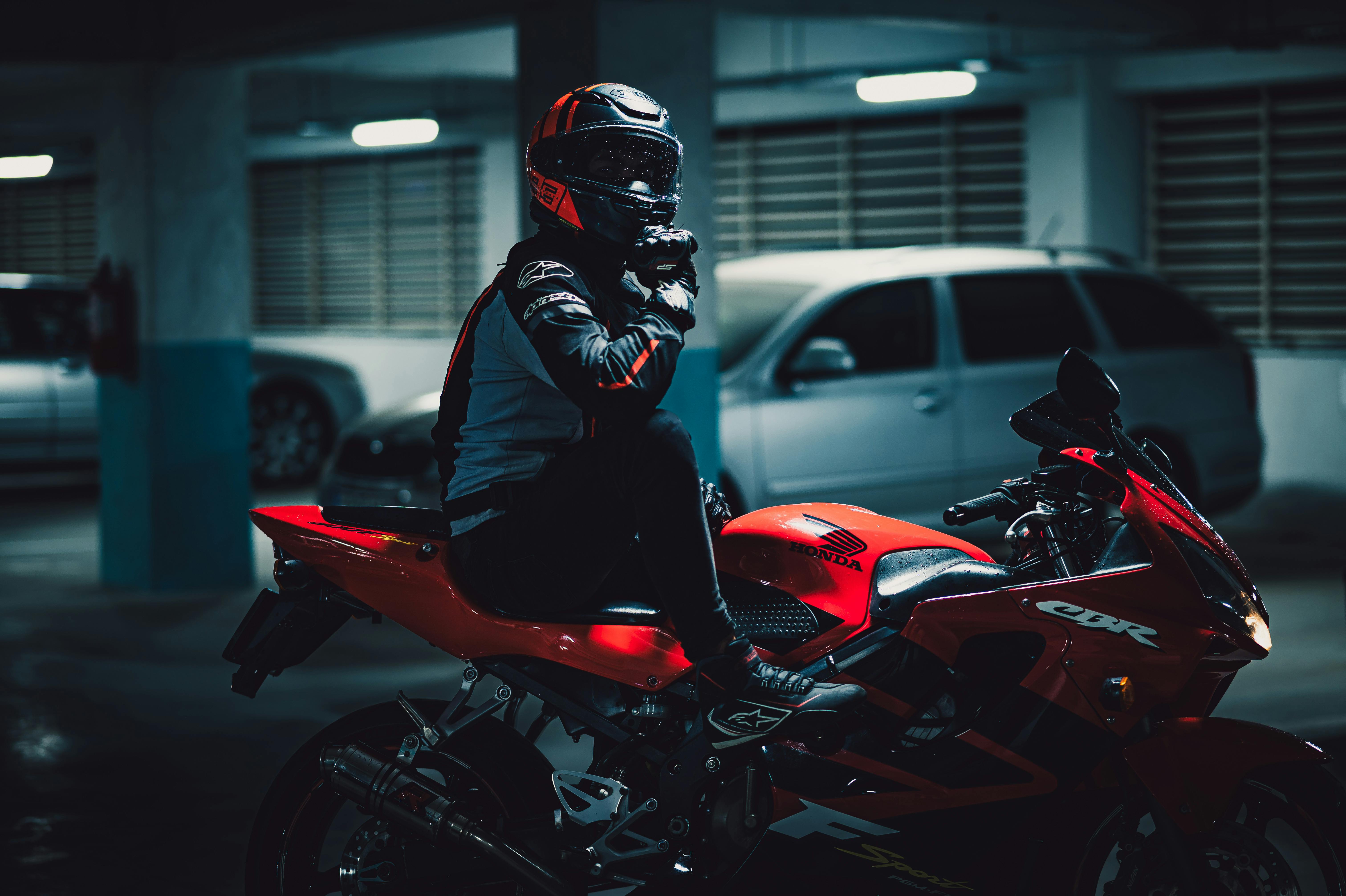 A motorcyclist with protective gear sitting on a red sport bike in a dimly lit parking garage.